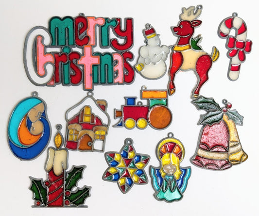 Colorful stained glass ornaments including the text Merry Christmas, a snowman with a broom, a reindeer saddled up to pull a sleigh, a beribboned candy cane, a train engine, a mother and child, a gingerbread house, two bells with holly, an angel with halo, a colorful star, and a lit red candle with holly leaves.