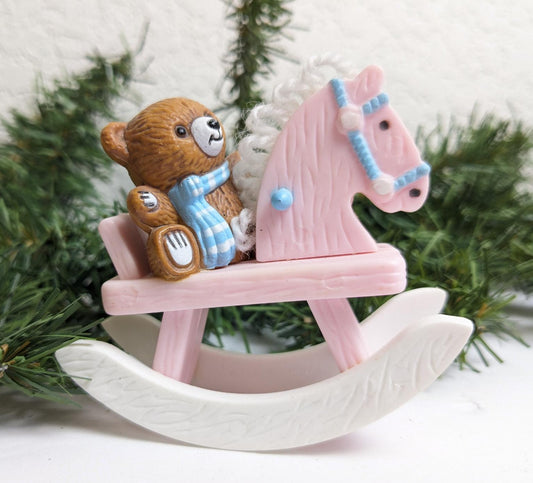This cute ornament of a teddy bear wearing a blue and white checkered scarf, sitting on a pink rocking horse with blue bridle, is a wonderful little gift for a new baby or expecting parents.