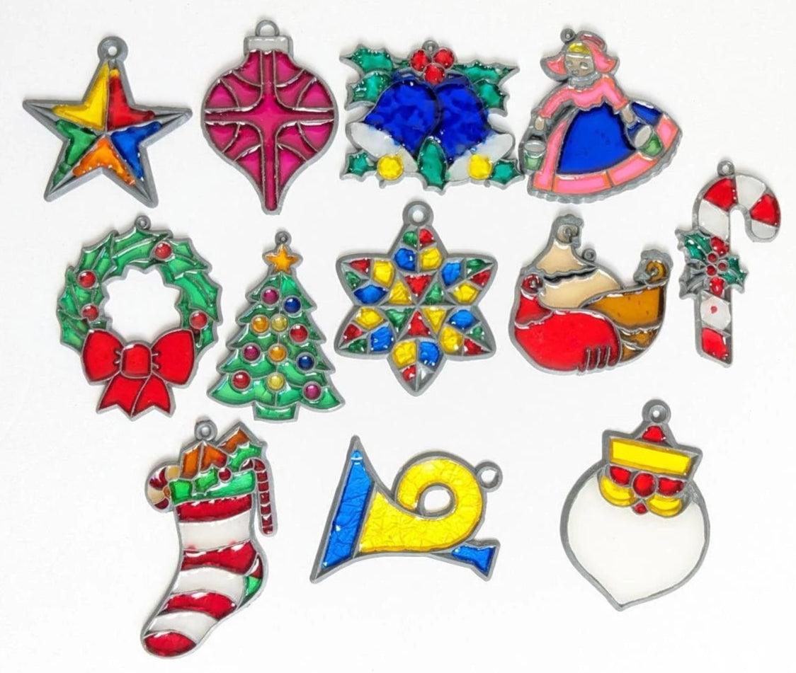 Faux stained glass holiday tree ornament collection including a colorful five pointed star, a red teardrop tree ornament, blue bells with hollly, a girl in a pink dress and blue apron, a hollyday pine bough wreath with red ribbon, a Christmas tree with colorful balls and yellow star, a multi colored six pointed star, a candy cane with holly berris, a white and red striped stocking with toys and holly, a yellow bugle and a santa with large white beard.