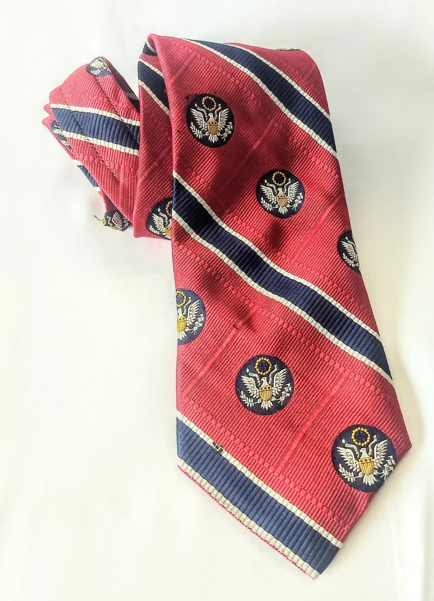 Red tie with smaller blue stripes bordered in very thin white stripes. Within the broad red stripes are blue circles with an American eagle.