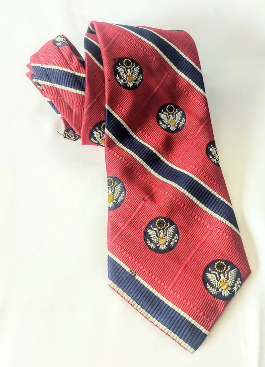 Red tie with smaller blue stripes bordered in very thin white stripes. Within the broad red stripes are blue circles with an American eagle.