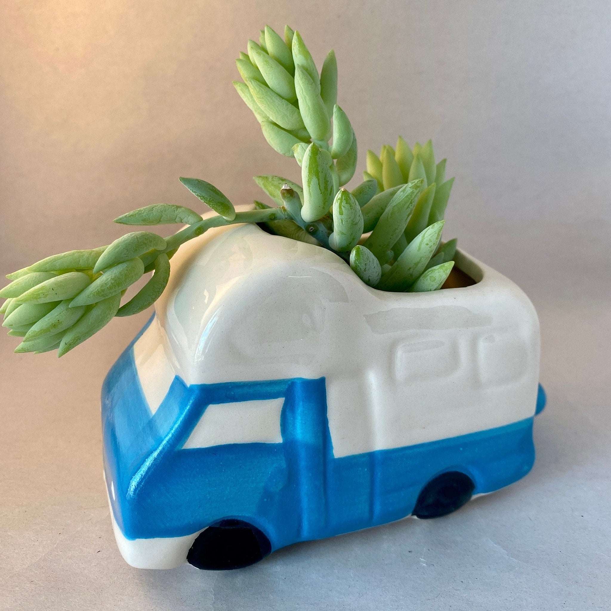 This cute glazed ceramic planter has a blue truck body with white camper shell, white windows and bumpers, and black tires. Its simplified look gives it a child-like whimsy and would look wonderful on a dresser or patio table.