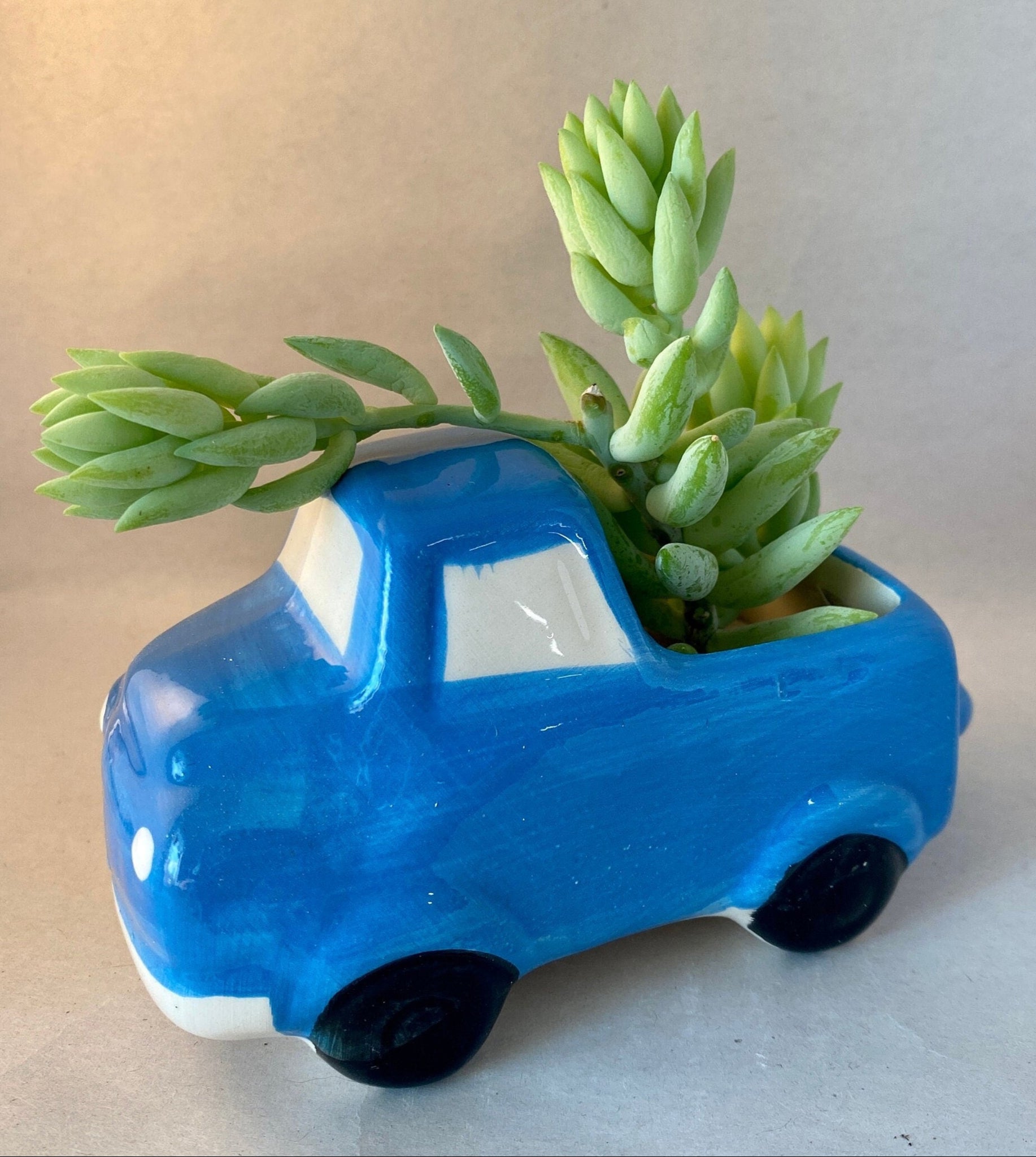 This glazed ceramic planter is five inches long with blue body, white windows and bumper and black tires. Its simpified look makes it reminiscent of a child's drawing.